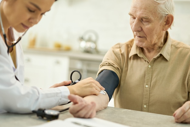 Homem idoso com manguito de manômetro em volta do braço sendo examinado por uma jovem médica
