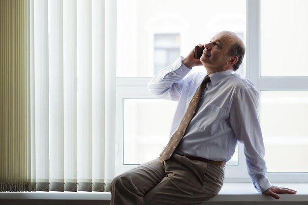 Homem idoso de camisa branca e gravata falando ao telefone Conversas importantes durante uma pausa no trabalho