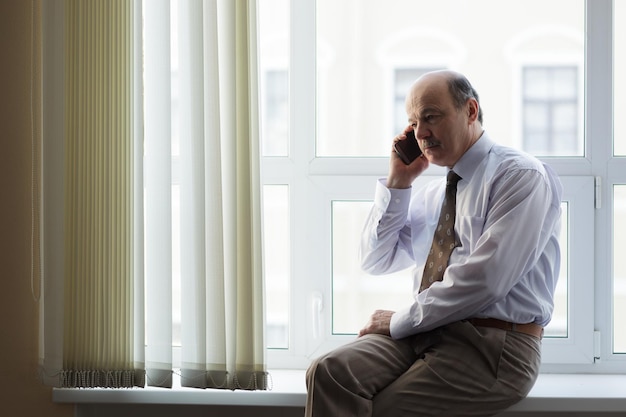 Homem idoso de camisa branca e gravata falando ao telefone Conversas importantes durante uma pausa no trabalho