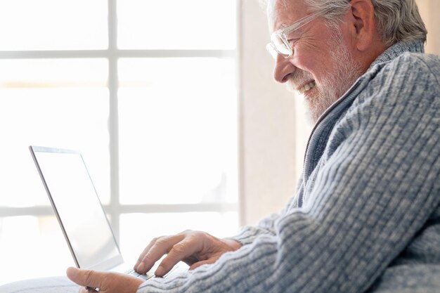 Homem idoso dos anos 70 sentado no sofá navegando no laptop sênior olhando para a tela do laptop navegando na rede geração mais antiga e conceito de uso fácil de aplicativo de tecnologia moderna