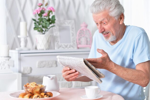 Homem idoso emocional a ler jornal em casa.