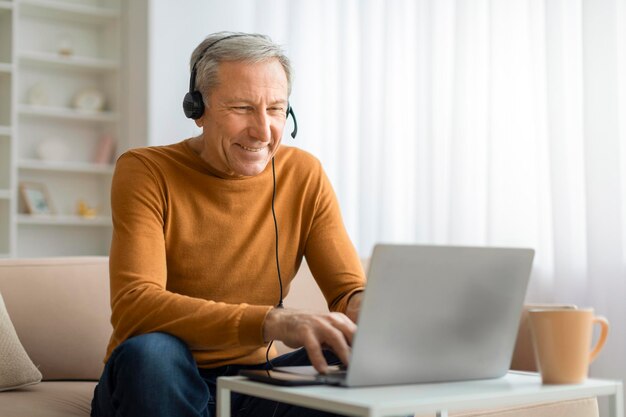 Homem idoso feliz com fone de ouvido usando laptop em casa