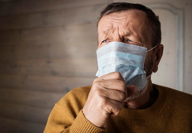Homem idoso frio com máscara médica tossindo