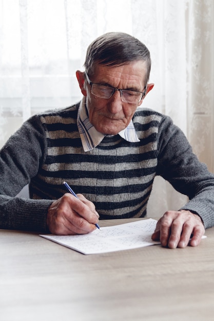 Homem idoso resolve sudoku ou palavras cruzadas