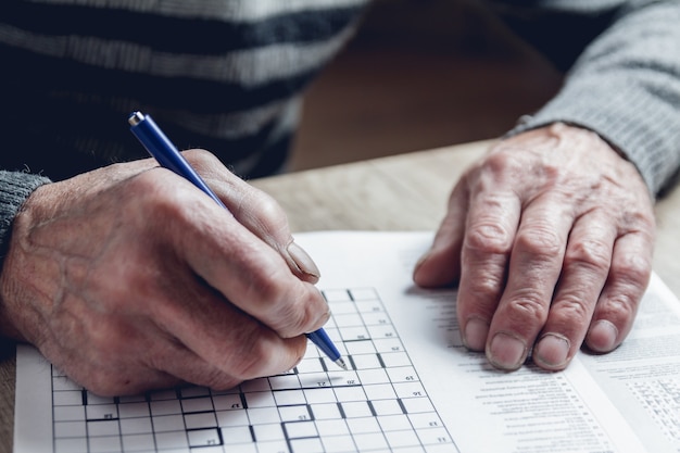 Homem idoso resolve sudoku ou palavras cruzadas