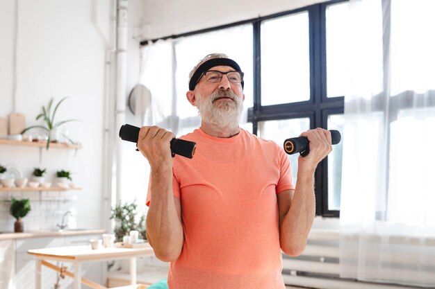 Homem idoso se exercitando com halteres durante o treinamento on-line Homem idoso pensionista treinamento saudável esporte de saúde em casa exercitando atividade física na idade avançada