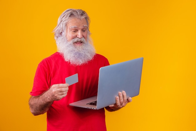 Homem idoso segurando o computador portátil e o cartão de crédito do banco. Transação de compras online. Método sem dinheiro de banco móvel.