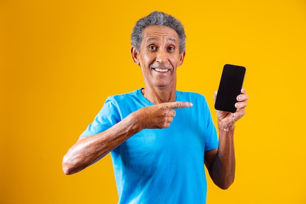 Homem idoso segurando o smartphone de tela em branco sobre fundo amarelo.