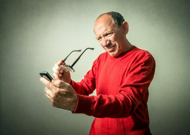 Foto homem idoso segurando telefone móvel contra a parede