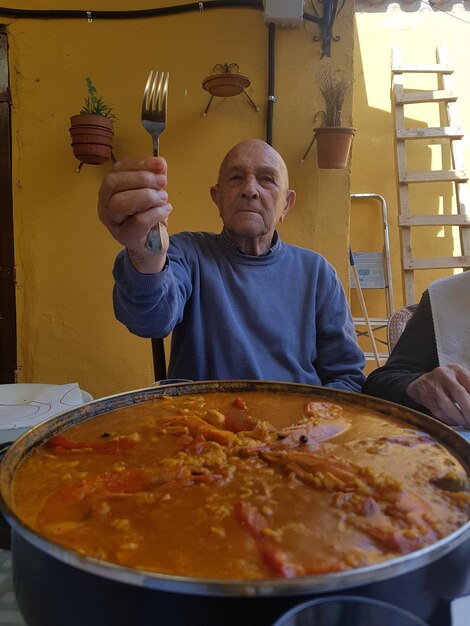 Foto homem idoso segurando um garfo enquanto está sentado com comida na mesa