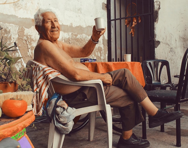 Foto homem idoso segurando uma xícara enquanto está sentado em uma cadeira