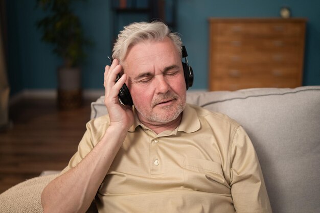 Homem idoso sentado no sofá na sala de estar cansado chefe relaxa no sofá ouvindo músicas