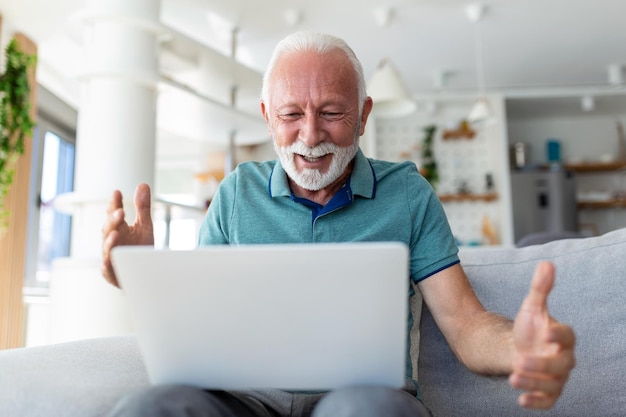 Homem idoso sentado no sofá olhando para a tela do laptop gritar com alegria se sente animado feliz comemorando a vitória na loteria momento de sorte tem oportunidades on-line de vendas e descontos conceito de comércio eletrônico