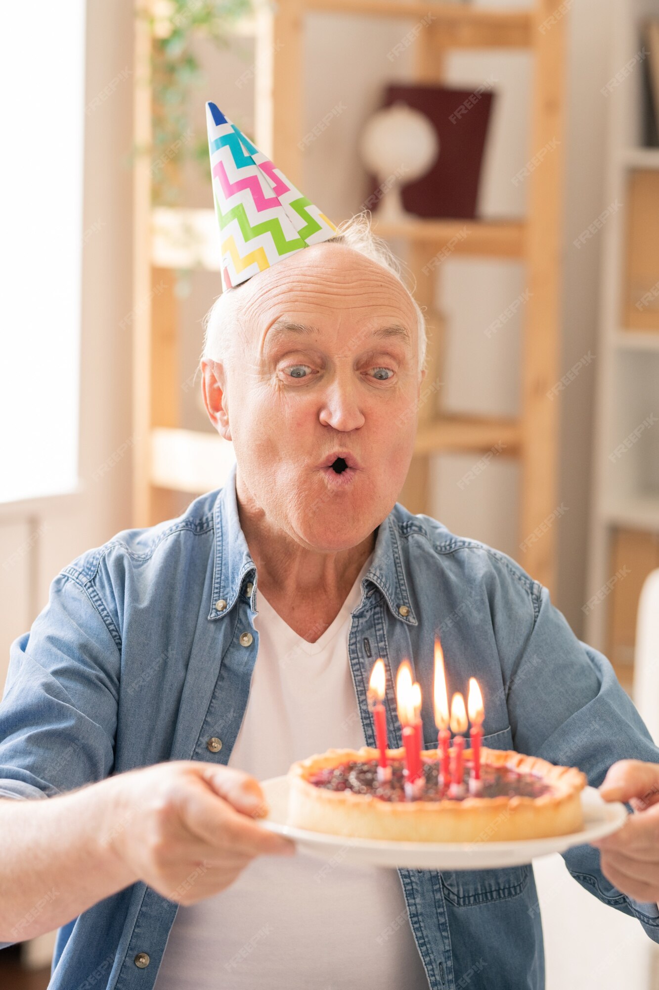 Close-up do homem adulto engraçado comemorando seu aniversário, segurando o  bolo bday com vela, soprando wistle festa e regozijando-se, em pé sobre  fundo azul claro.