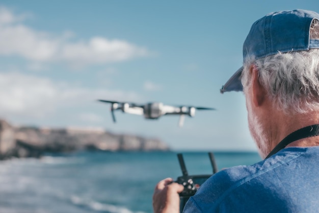 Homem idoso voando com drone ao pôr do sol usando controle remoto de tablet digital Fotografias aéreas no mar