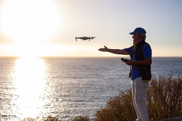 Homem idoso voando com drone ao pôr do sol usando controle remoto digital Fotografias aéreas Mar