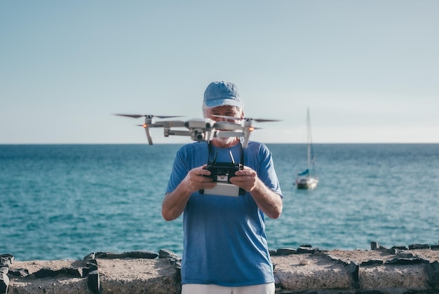 Homem idoso voando com drone ao pôr do sol usando controle remoto Fotografias aéreas Mar em fundo