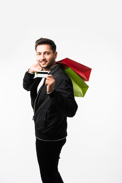 Homem indiano asiático mostrando sacolas de compras e cartão de crédito ou débito em pé sobre um fundo branco