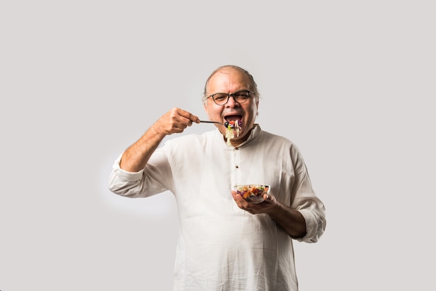 Homem indiano asiático sênior comendo salada verde fresca. Macho maduro comendo lanche saudável, saúde, conceito de dieta