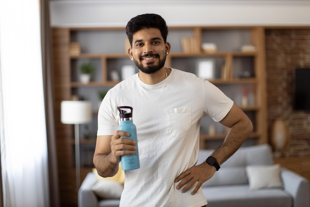 Homem indiano com garrafa de água posando na sala de estar