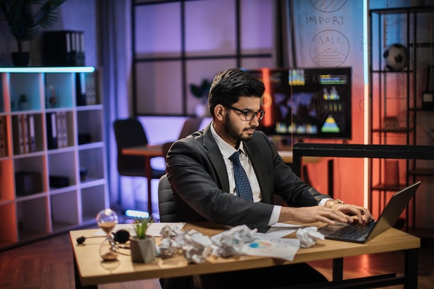 Homem indiano com roupa formal, sentado à mesa e usando laptop sem fio