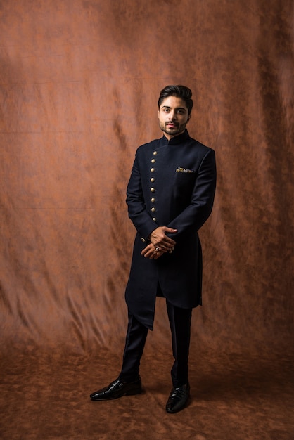 Homem indiano com roupa tradicional OU kurta, roupas de pijama. Modelo de moda masculina em Sherwani, posando ou em pé contra um fundo marrom grunge, foco seletivo