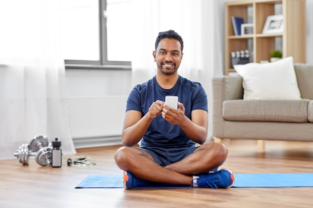 homem indiano com smartphone em tapete de exercício em casa