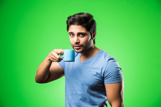 Homem indiano com uma xícara de chá ou café ou uma caneca. Bebendo, apresentando ou segurando enquanto está isolado