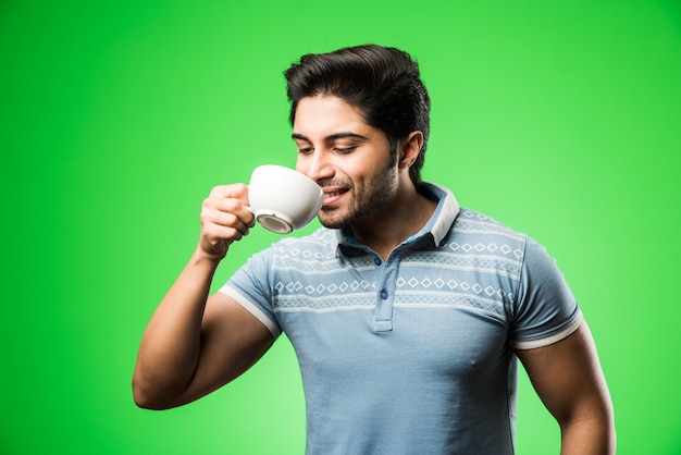 Homem indiano com uma xícara de chá ou café ou uma caneca. Bebendo, apresentando ou segurando enquanto está isolado