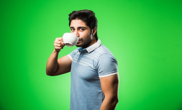 Homem indiano com uma xícara de chá ou café ou uma caneca. Bebendo, apresentando ou segurando enquanto está isolado