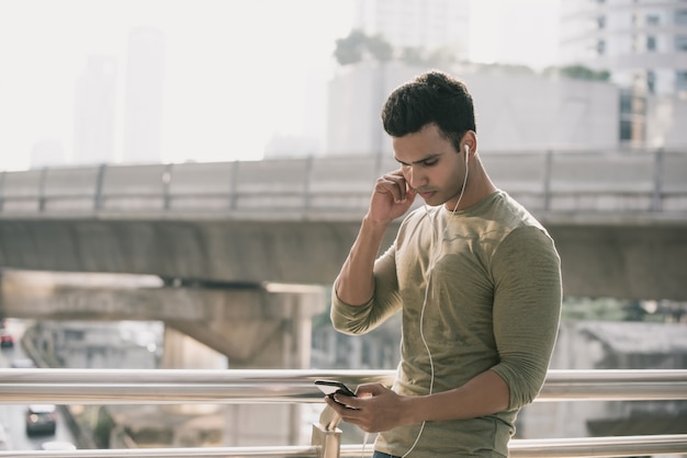 Homem indiano considerável novo que veste fones de ouvido que escuta a música