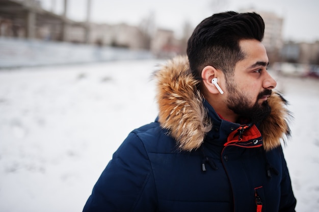 Homem indiano de barba usar jaqueta em um dia frio de inverno. Fones de ouvido móveis nos ouvidos.