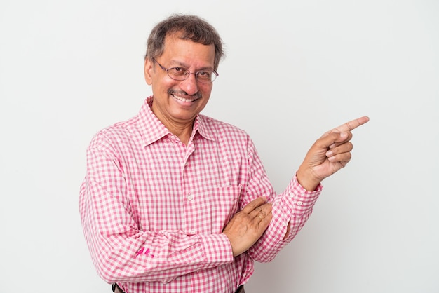 Foto homem indiano de meia idade, isolado no fundo branco, sorrindo alegremente, apontando com o dedo indicador para longe.