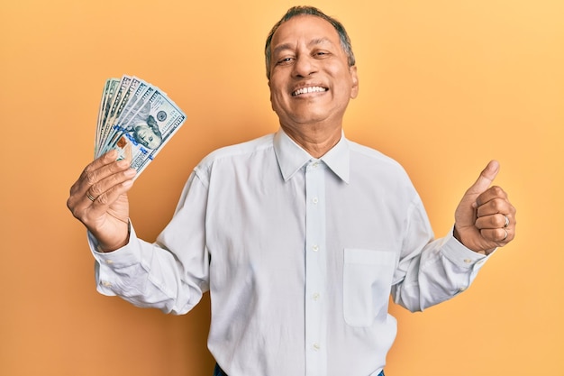 Homem indiano de meia-idade segurando dólares gritando orgulhoso comemorando a vitória e sucesso muito animado com o braço erguido