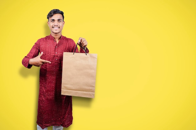 Homem indiano em roupas étnicas com sacolas de compras isoladas sobre fundo amarelo
