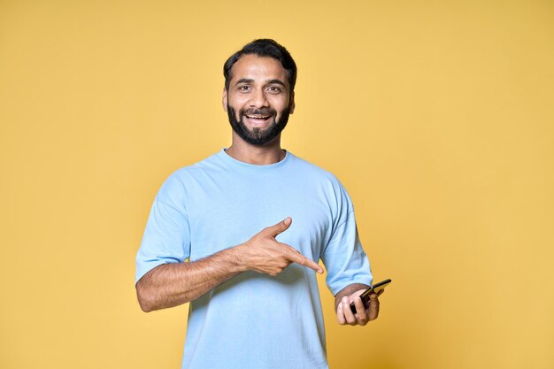 Foto homem indiano feliz apontando para o celular isolado em fundo amarelo