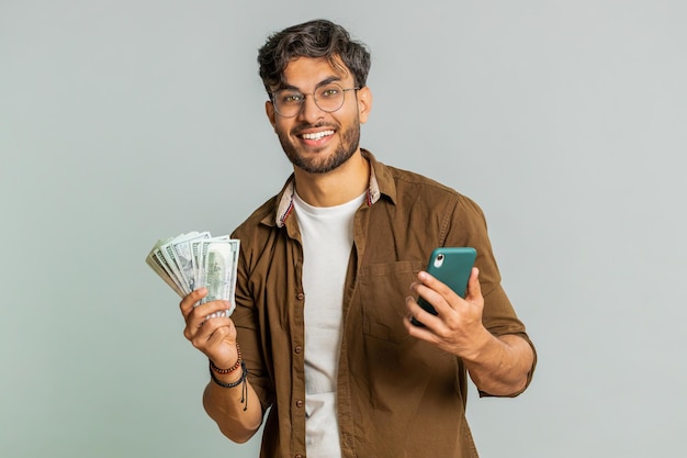 Homem indiano feliz usa smartphone alegrando-se de ganhar um jogo recebendo dinheiro dólar em dinheiro celebrando o sucesso