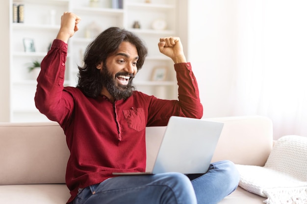 Foto homem indiano millennial emocional olhando para a tela do laptop gesticulando