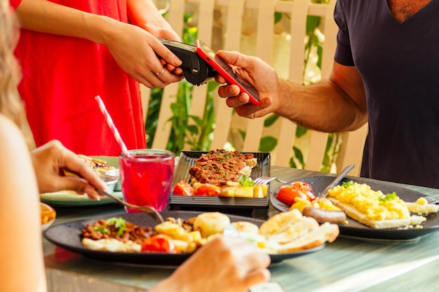 Homem indiano pagando no restaurante por aplicativo de cartão de crédito no leitor de smartphone