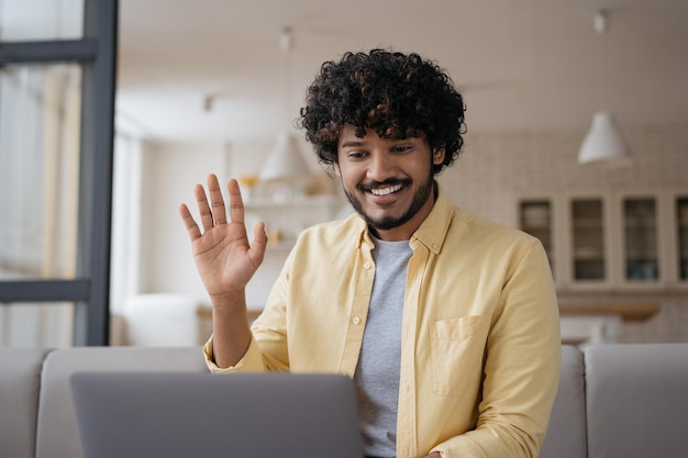 Homem indiano sorridente tendo chamada de vídeo acenando com a mão Comunicação freelancer online trabalhando em casa