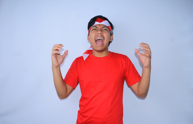 Homem indonésio irritado gritando e apertando as mãos vestindo camiseta vermelha no dia da independência da indonésia