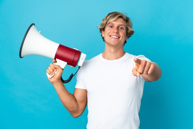 Homem inglês sobre fundo azul isolado segurando um megafone e sorrindo enquanto aponta para a frente