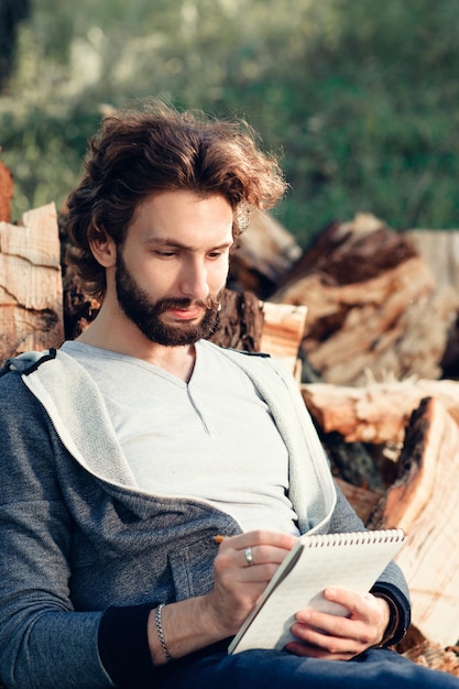 Homem inspirado escrevendo no caderno no bando de lenha.