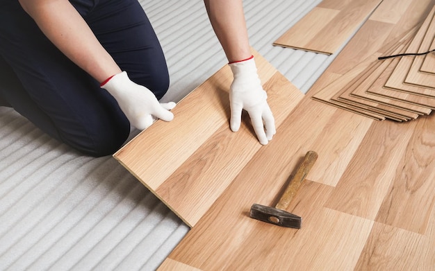 Homem instalando piso laminado, detalhe em telha de madeira sendo instalada, sobre camada de base de espuma branca.