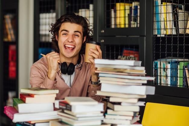 Foto homem intelectual lendo um livro sentado na biblioteca em frente a estantes com uma xícara de café