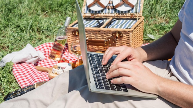 Foto homem irreconhecível em calças brancas do lado de fora fazendo piquenique e usando laptop trabalhando ao ar livre