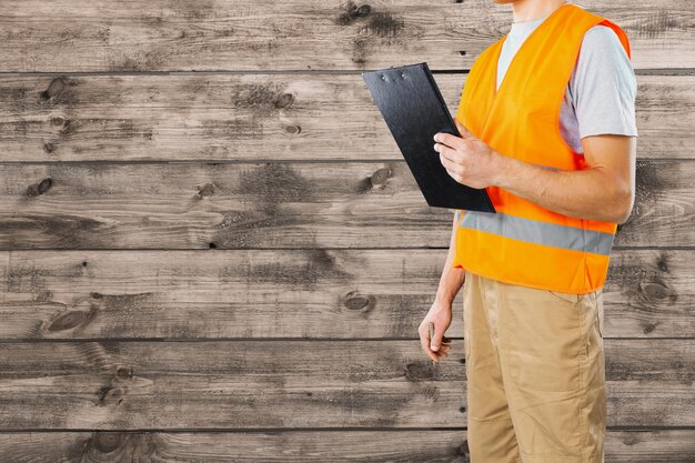 Homem irreconhecível, trabalhador da construção civil, segurando uma pasta na mão no fundo de madeira