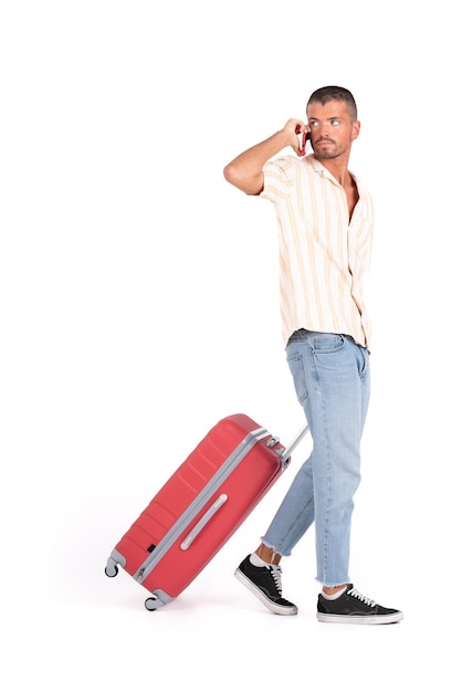 Foto homem isolado com uma mala de viagem vermelha andando e falando no celular em um fundo branco