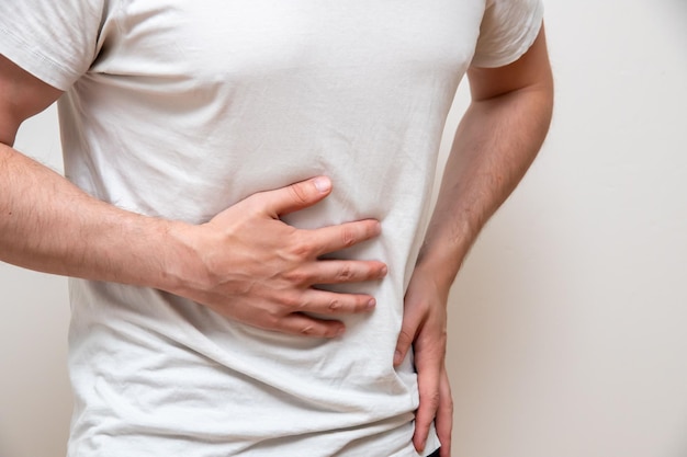 Homem, isolado em um fundo azul, segurando a barriga com uma mão com dor