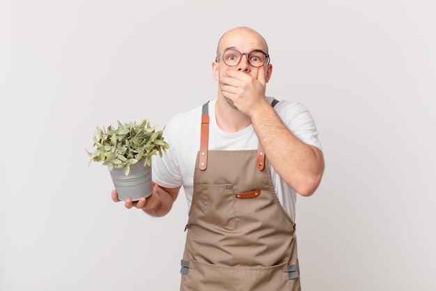 Homem jardineiro cobrindo a boca com as mãos com uma expressão chocada e surpresa, mantendo um segredo ou dizendo oops